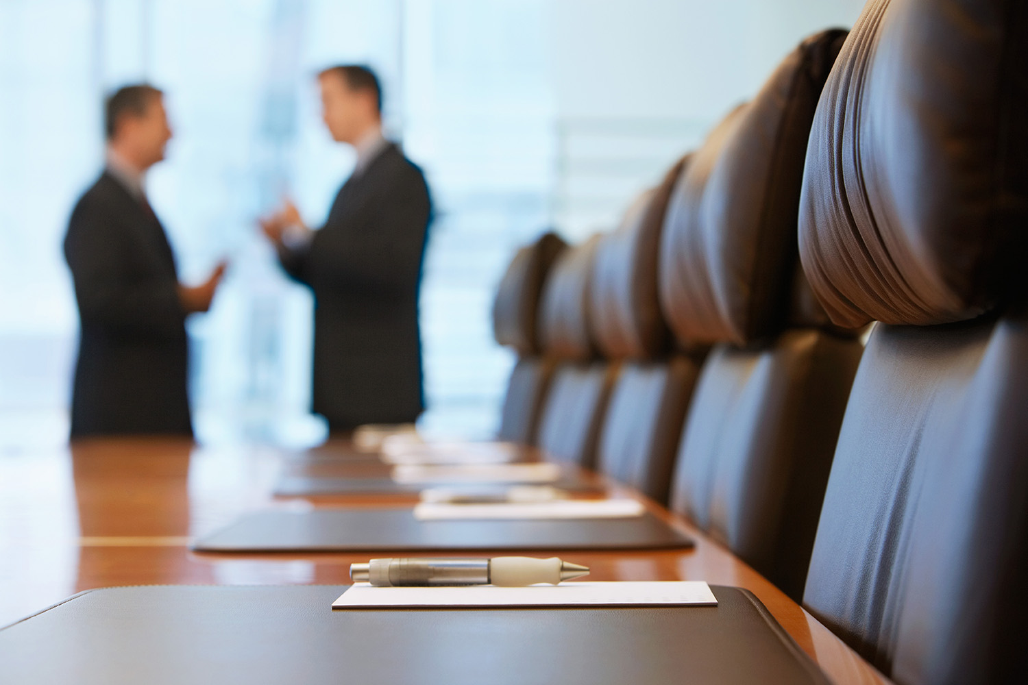 Blurred outline of two men talking at the end of a long boardroom tableT